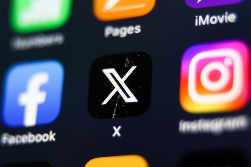 Na displeji telefonu se zobrazují ikony Facebook, X a Instagram.
